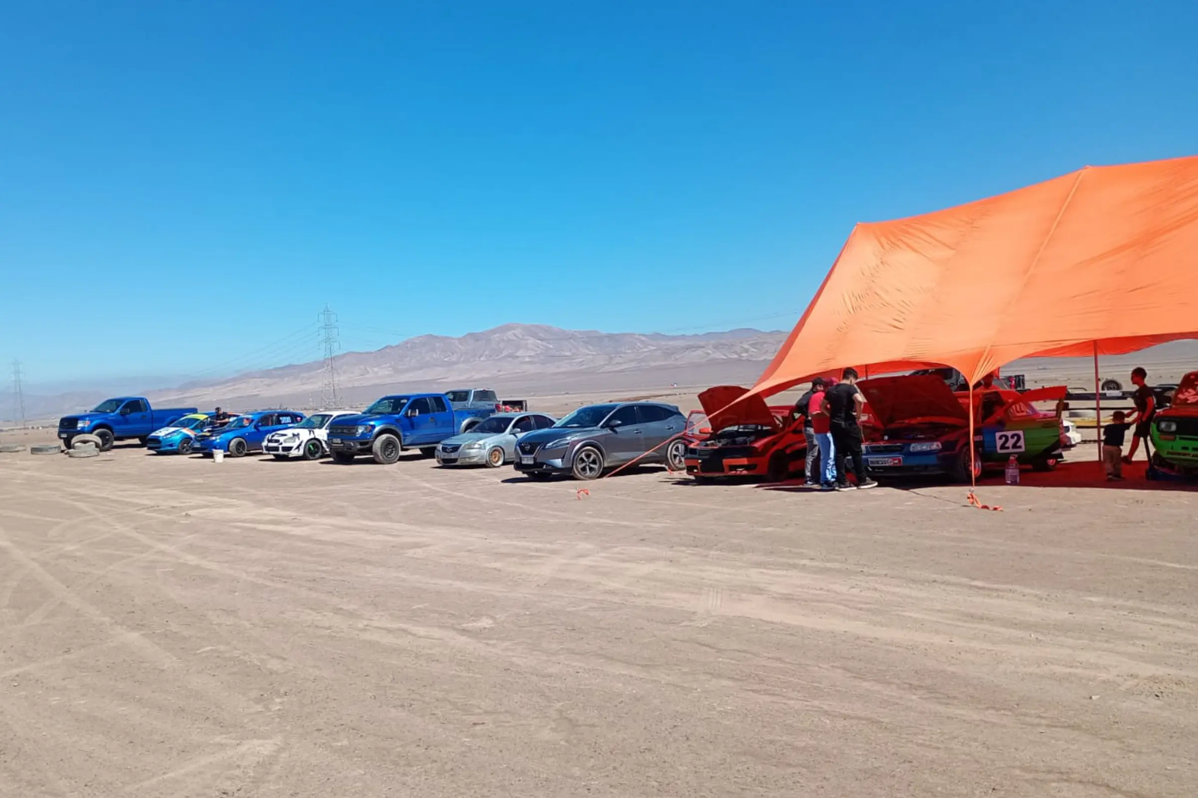 Paddock con vehículos y carpa naranja en el desierto
